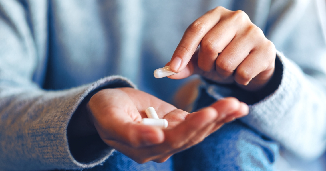 A set of hands holding three white capsules.