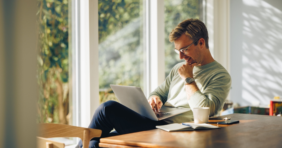 A man sitting inside in the sun on his laptop.