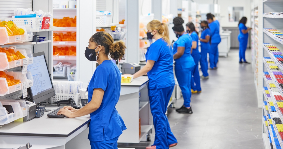 A row of technicians in blue scrubs working at individual work stations.