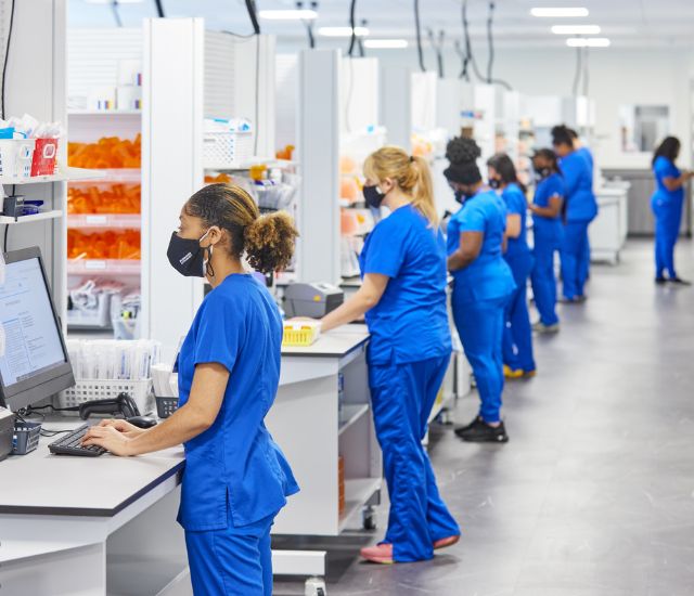 A row of technicians in blue scrubs working at individual work stations.