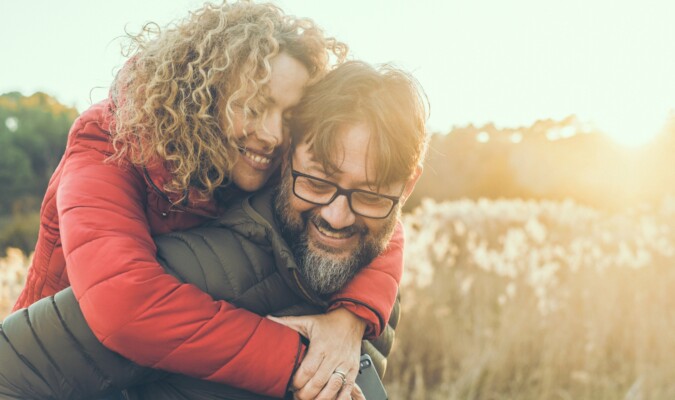 A woman on a mans back both smiling outside.