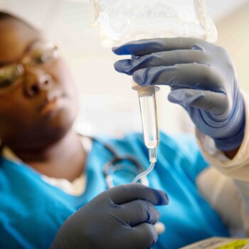 A nurse in protective gear preparing an IV bag.