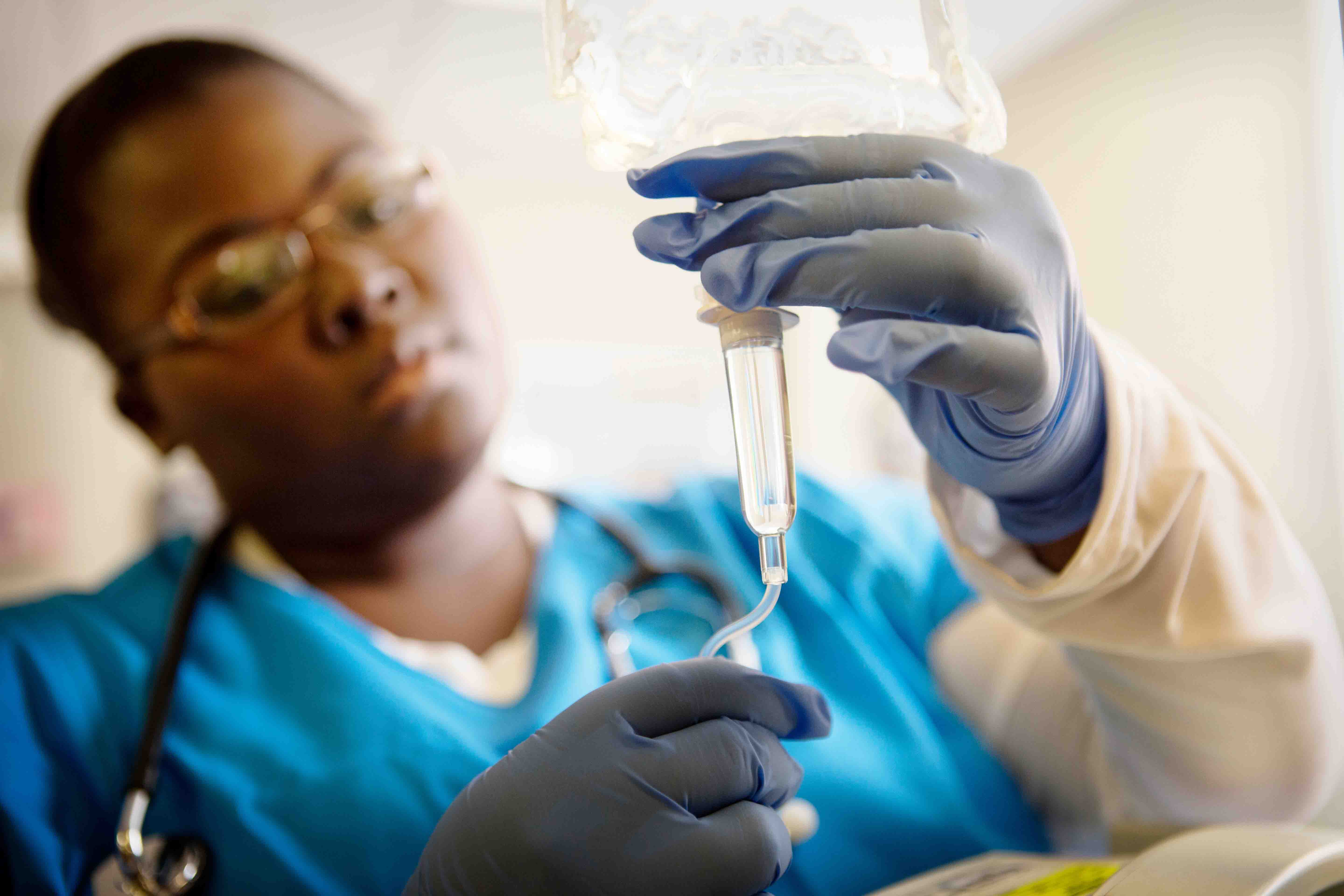 A nurse in protective gear preparing an IV bag.