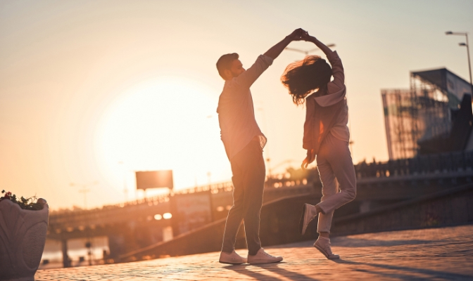 A man and woman dancing outdoors with the sunset in the background.