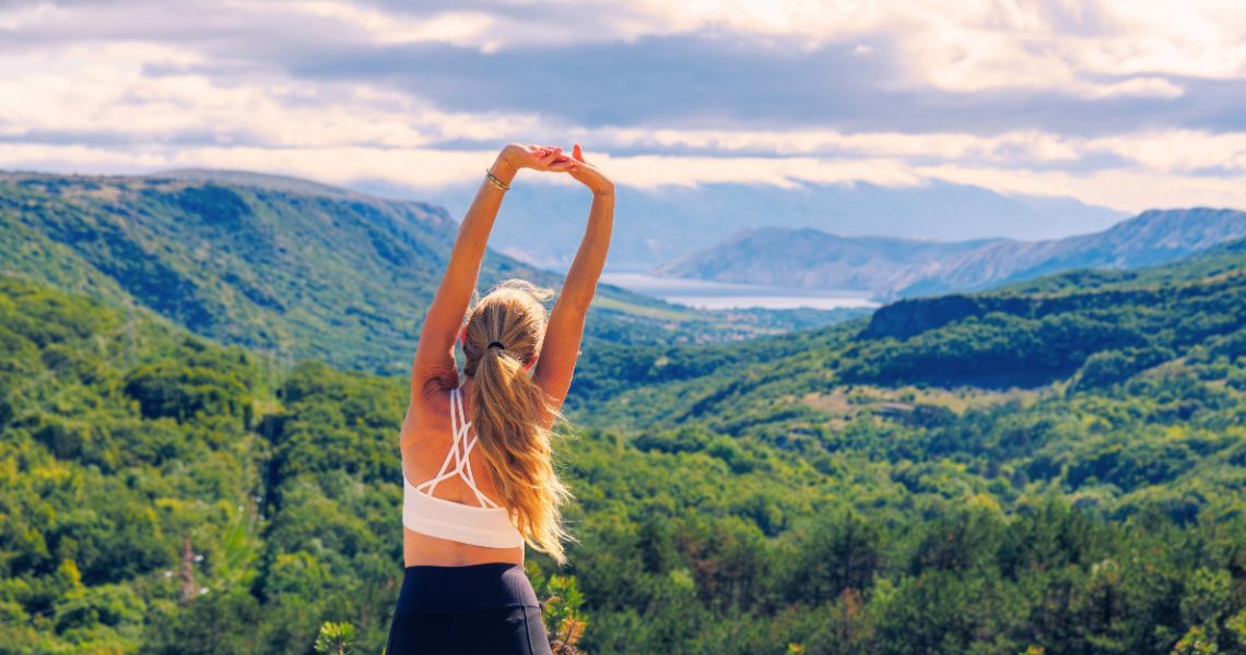 Woman in workout attire stretching facing mountains.