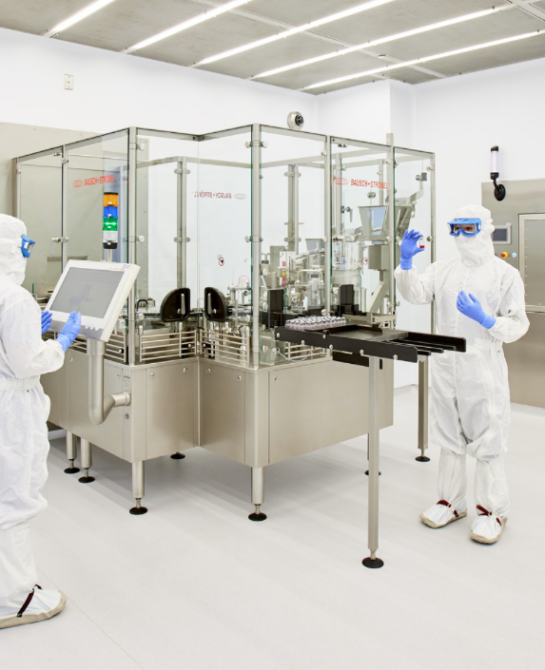 Two workers in white clean suits working on a machine.